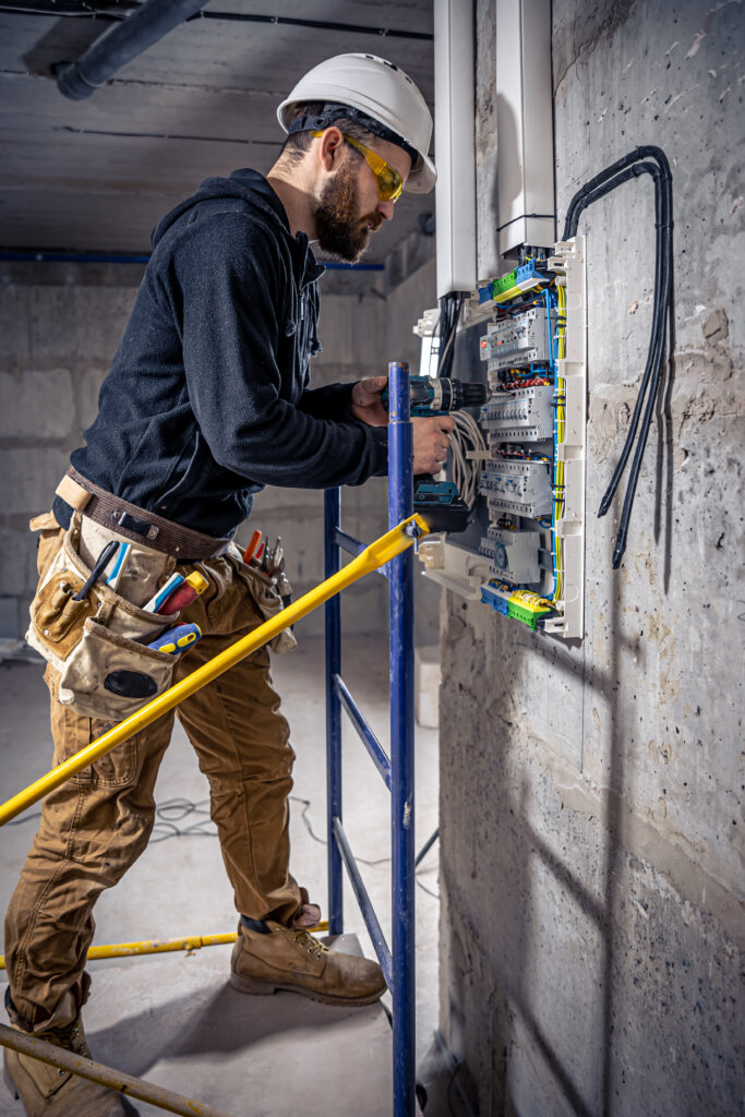 A male electrician works in a switchboard with an electrical connecting cable.